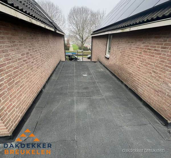 Plat dak met bitumen dakbedekking tussen bakstenen muren in Breukelen Plat dak met bitumen dakbedekking tussen bakstenen muren in Breukelen